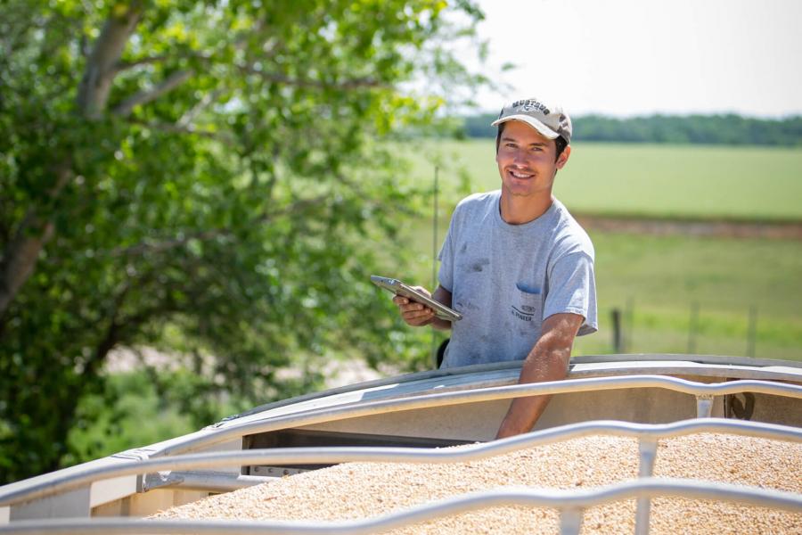 A student stands at the top of a grain truck taking samples.