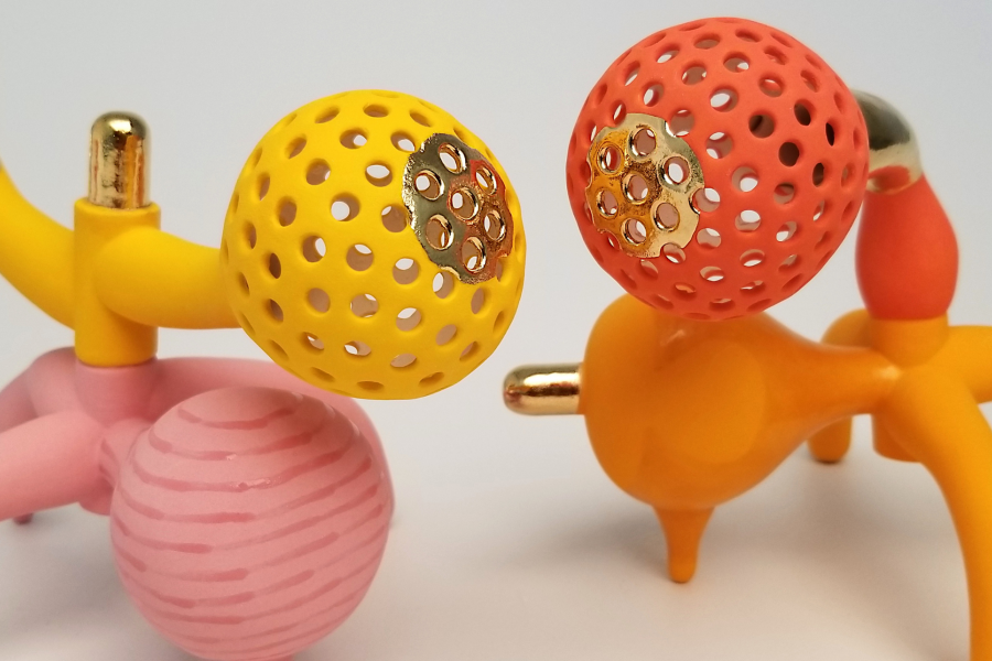 Two colourful orange, yellow, pink, and metallic gold organic sculptures on a white background