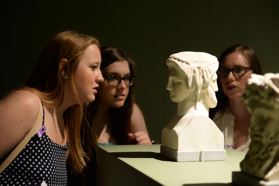 Three students look at an artifact on display.