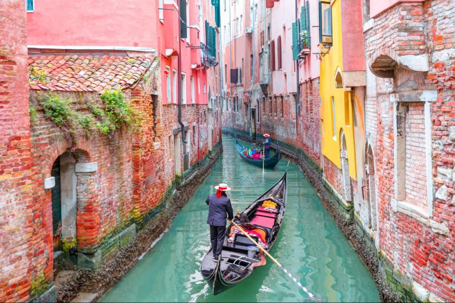 Gondola on narrow canal lined by pink buildings.