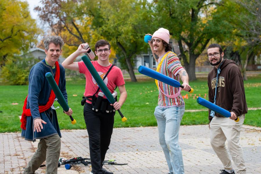 Four people in costume holding foam swords toward the camera.