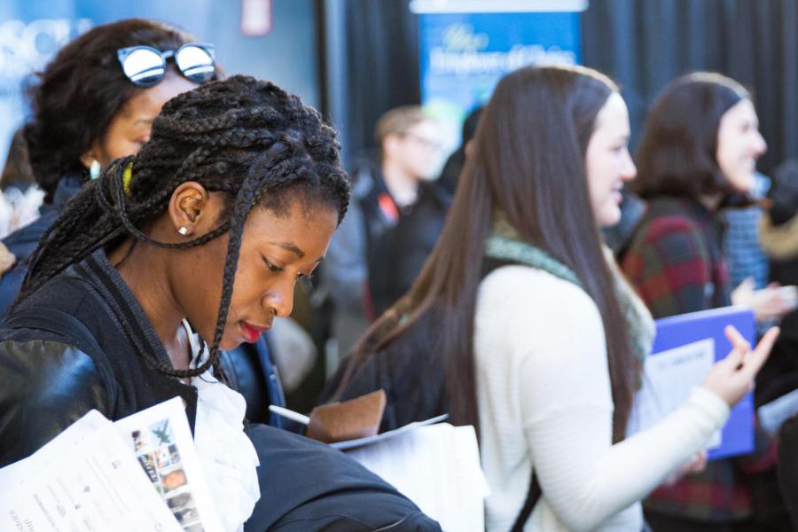 Students gathered at the annual career fair. A woman in the foreground reviews printed information she is holding. 
