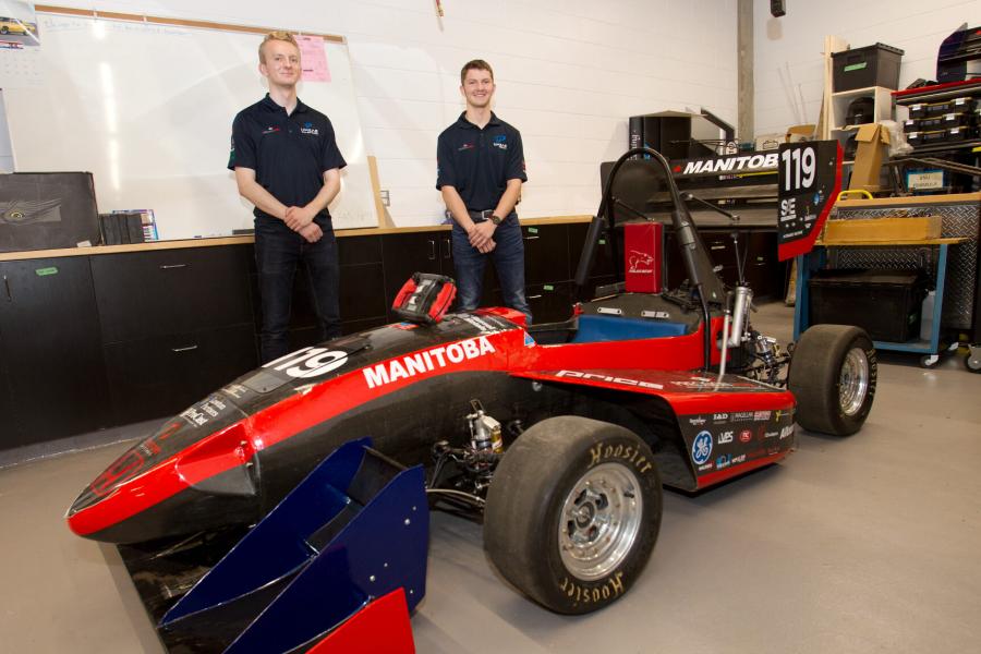 Two mechanical engineering students stand behind a small racing car they have built.