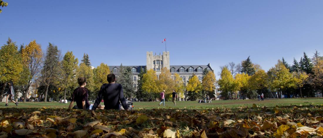 Students sitting outside in the quad surrounded by fall colours. 