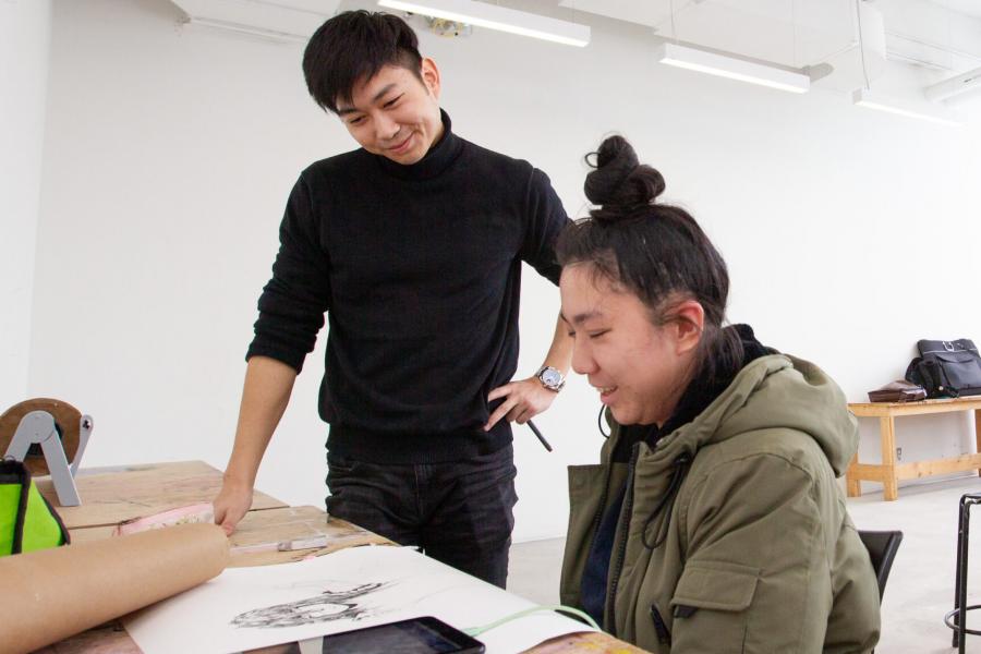 A smiling student looks at another students drawing work.