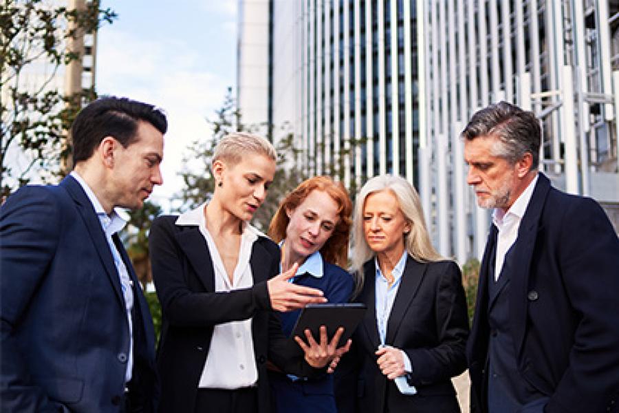 A businesswoman holding a tablet while discussing with her colleagues outside the building.