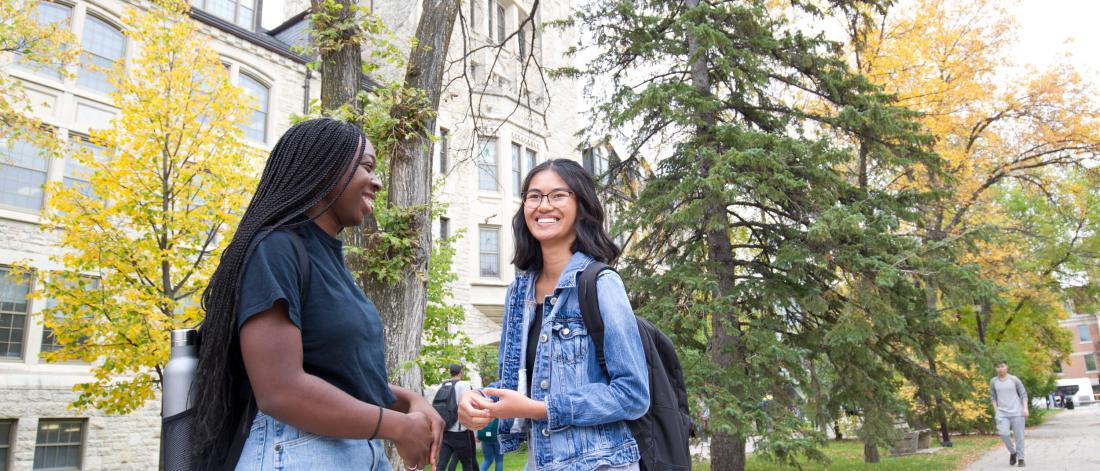 Two students stand together talking outside of the Tier building at the University of Manitoba Fort Garry campus. 