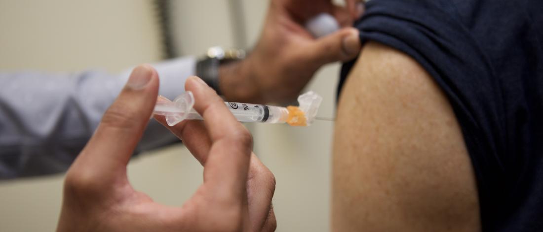 A close up view of someone administering a flu shot into someone's forearm.