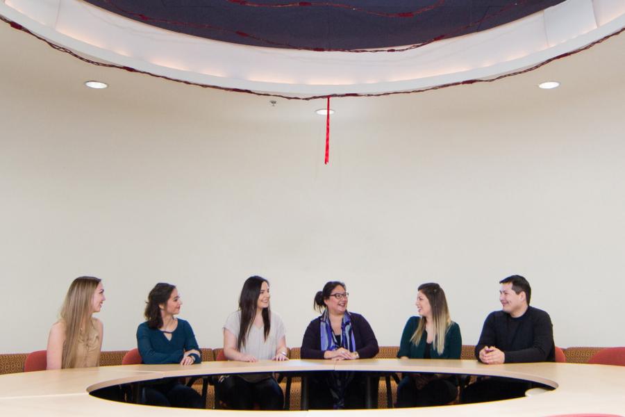 Indigenous student advisor Carla Loewen sits at a circular table with several students at Migizii Agamik. 