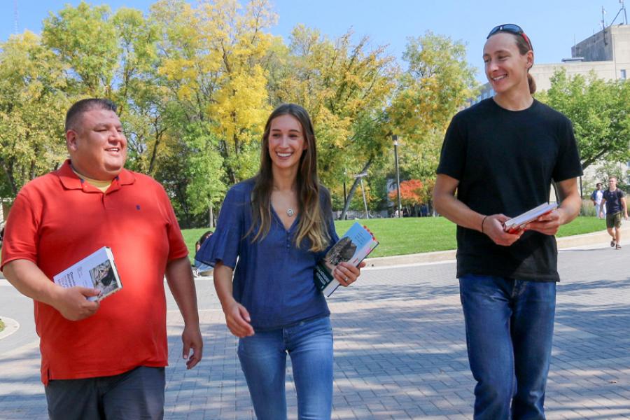 Two men and a woman walk across campus with textbooks.