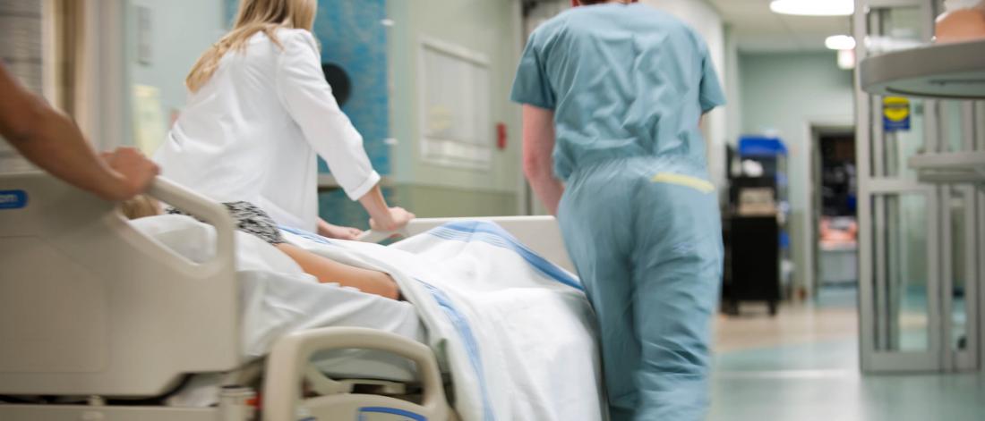 Three emergency department doctors push a patient down a hallway in a gurney.