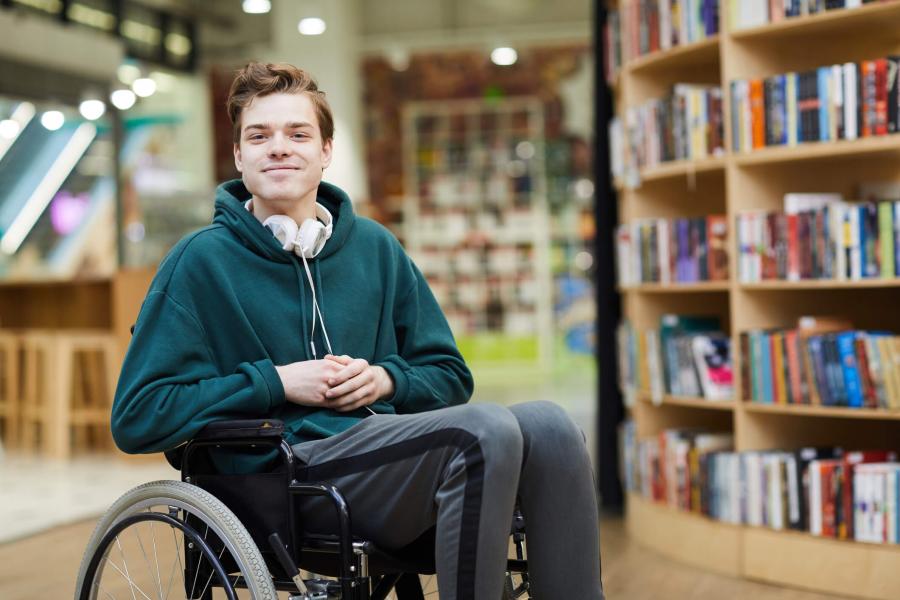 Young man in a library, seated in a wheelchair.
