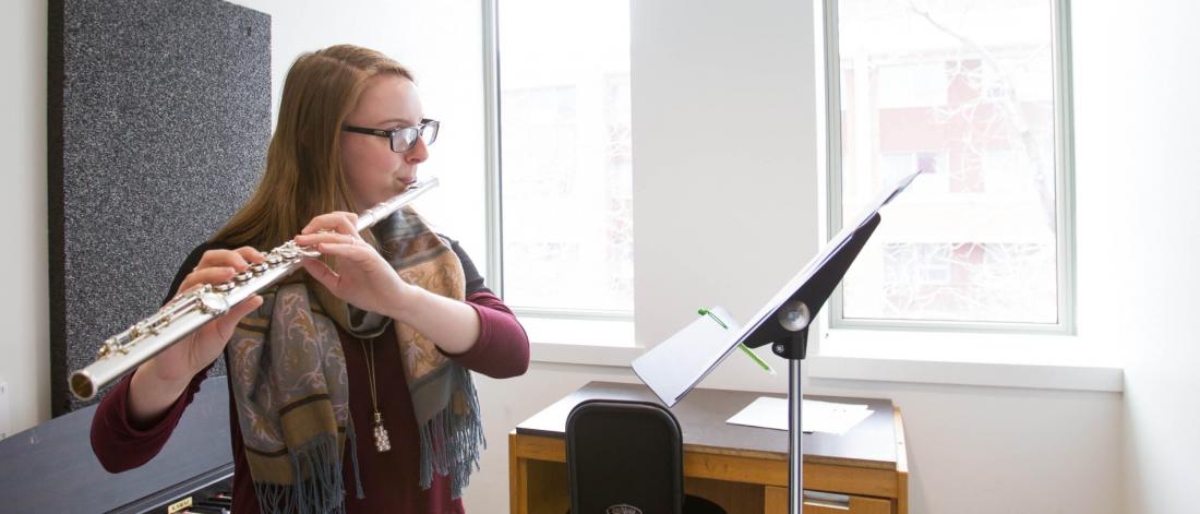 A music student practices the flute in a practice room. 