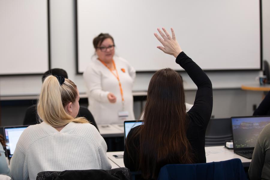 A classroom of Master of Nursing program students watch a presentation on a projector screen.