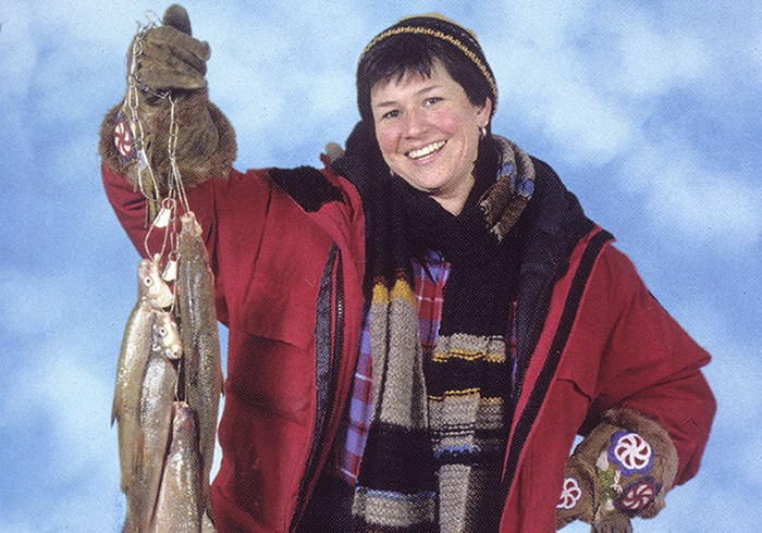 Smiling woman dressing in winter clothes holds up string of fish.