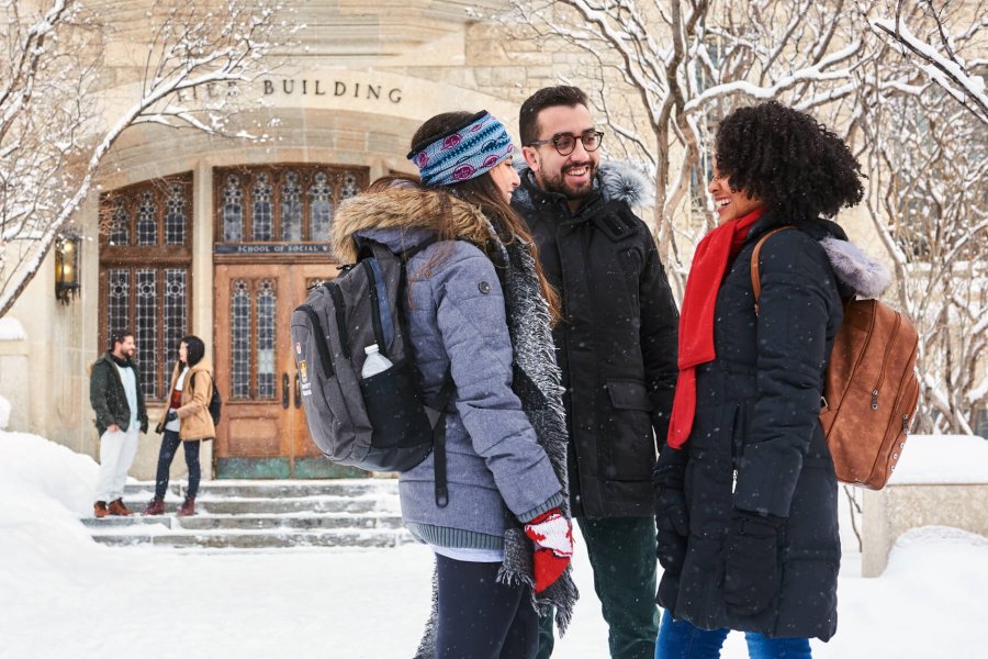 Three smiling international students talking outdoors on a snowy winter day.