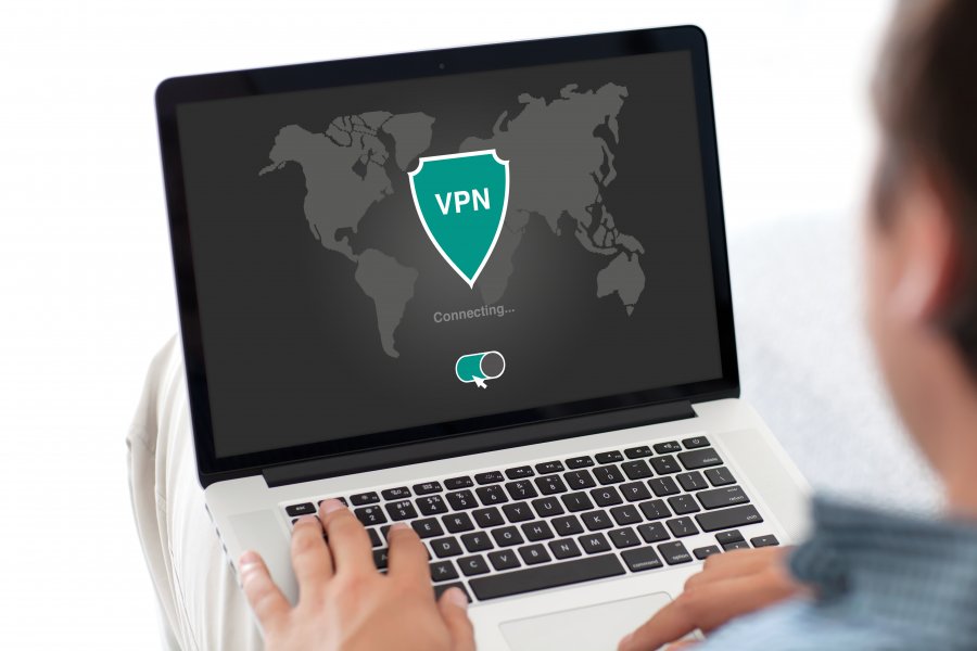 Man working on a laptop with a world map shown on and an shield symbol overlaid with VPN written across