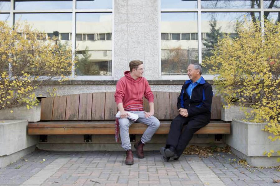 A Metis student sits on a bench and talks with Elder-in-Residence Norman Meade.