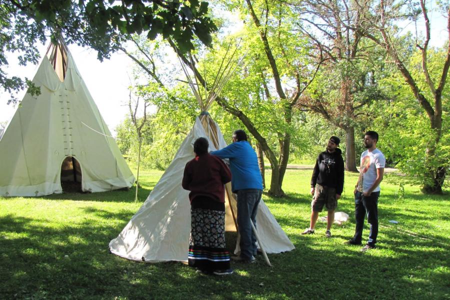 Indigenous knowledge keepers demonstrating how to construct a teepee.