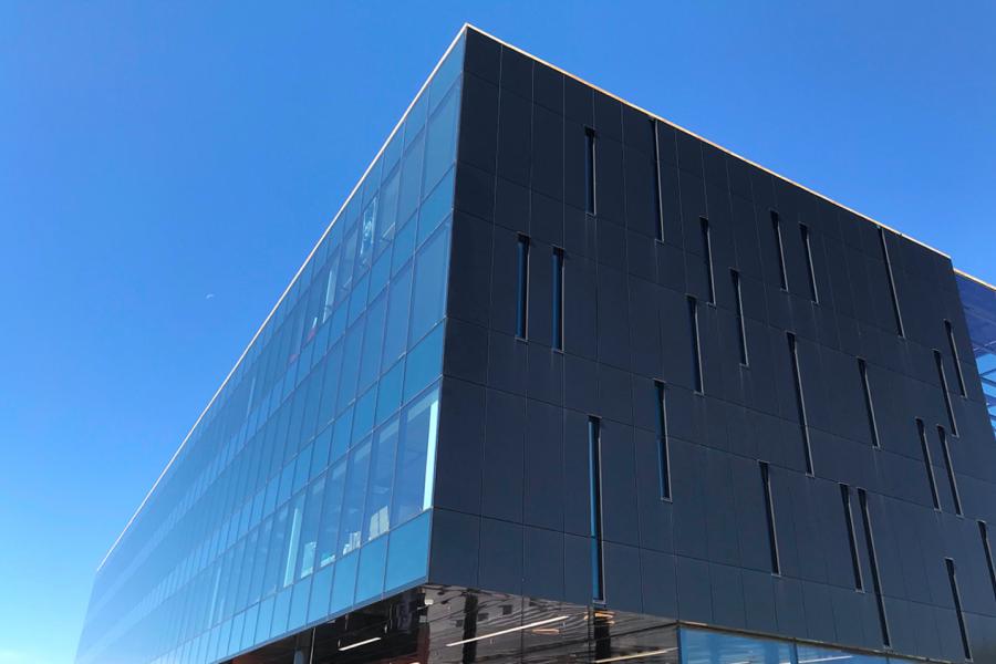 The dark rectangular glass exterior of the Innovation Hub building captures the reflection of the bright blue sky.