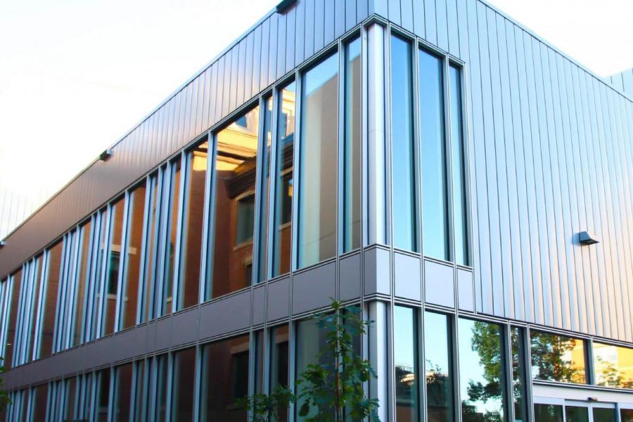 Exterior view of the Tache Arts building, its large glass windows filled with the reflection of the surrounding trees and sunset.