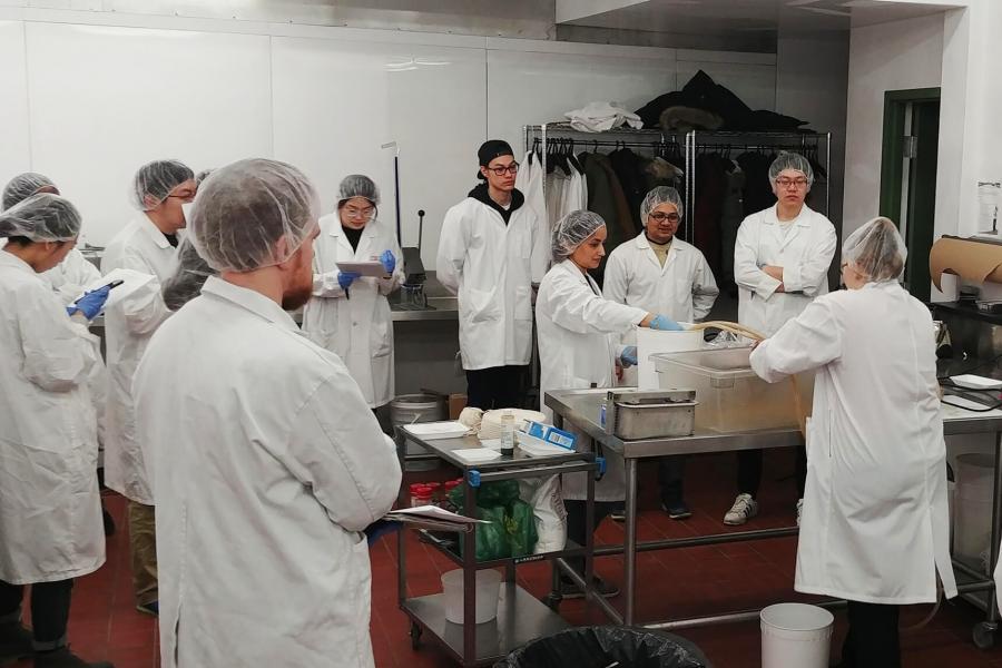 Students in labcoats listen to food science instructor. 