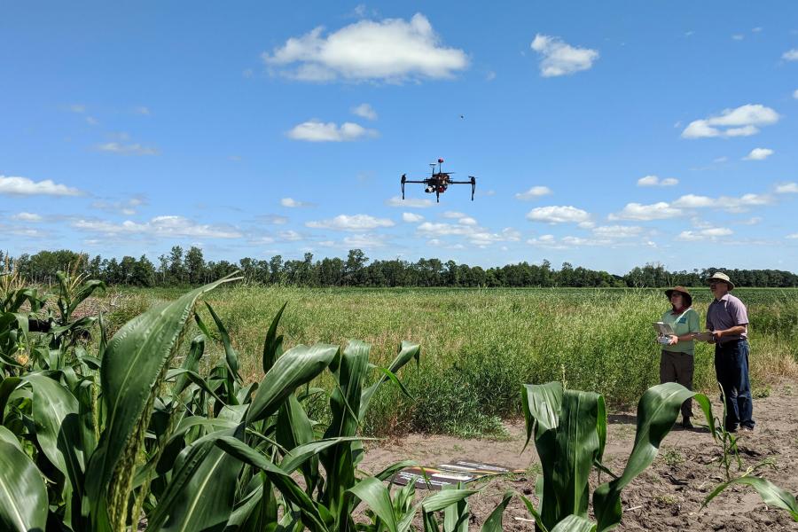 2 people watch a drone fly over a field