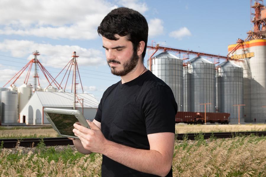 A person uses a tablet in front of silos on a rail line