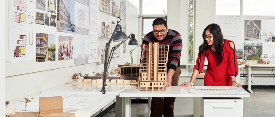 Two students review an architectural model together in a classroom setting.