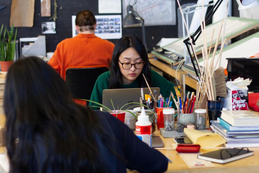 Students sit at their desks working on projects with various supplies and tools.  