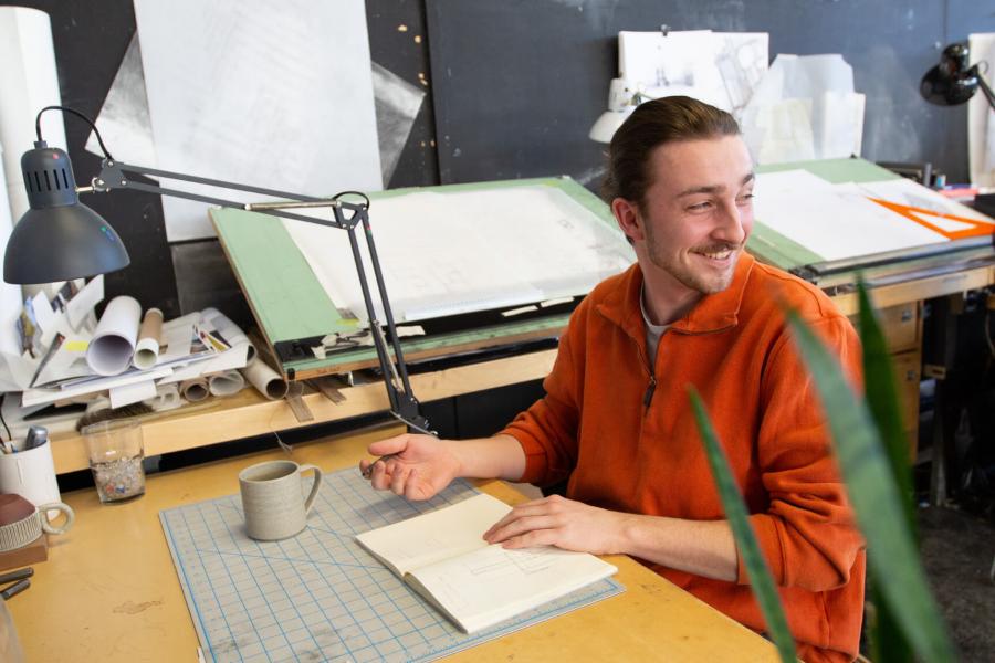 an environmental design student smiles while working at his desk.