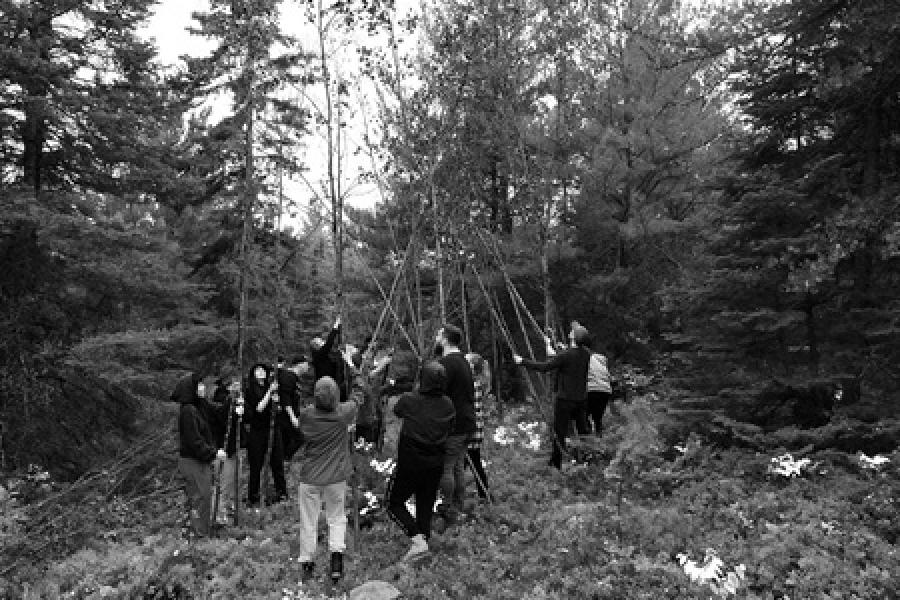 group of individuals in a forrest setting up a structure with tree trunks