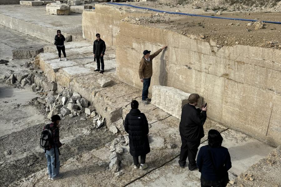 Group of people examining a stone quarry with large rock formations and a clear blue sky in the background.
