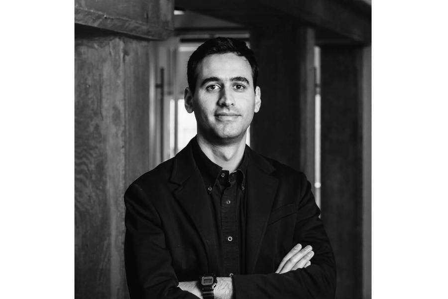 Black and white portrait of a person in a hallway with arms crossed.