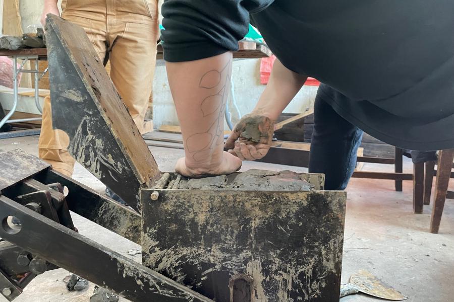 Hands working with clay on a black metal machine in a workshop.