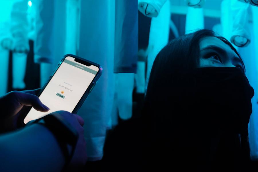 Person in a blue-lit room with suspended cylinders and a smartphone displaying an interface.