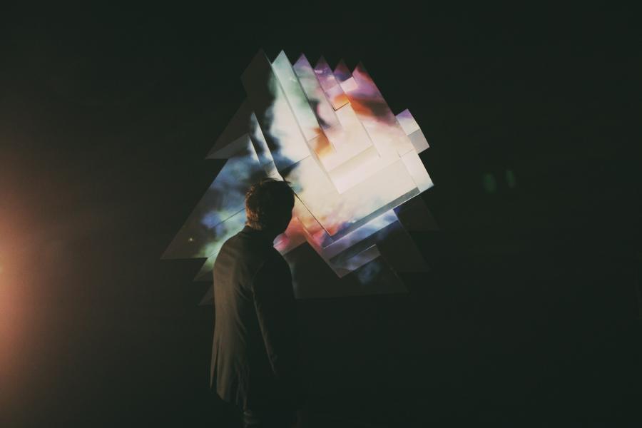 Person facing geometric shapes with cosmic patterns in a dark setting.
