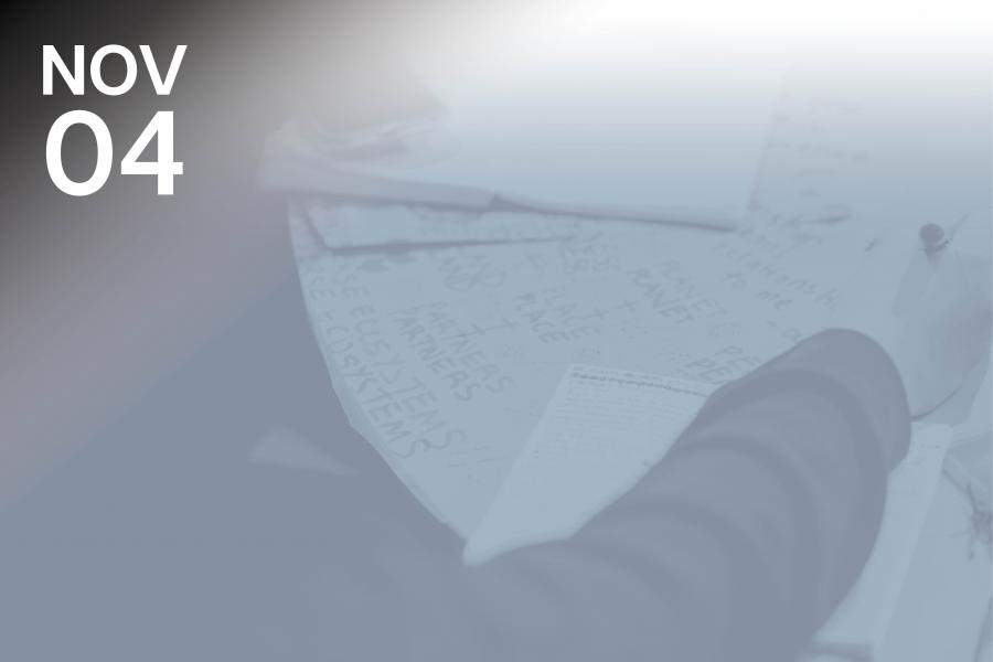 Blurred image of a person writing at a table covered with papers and notes.