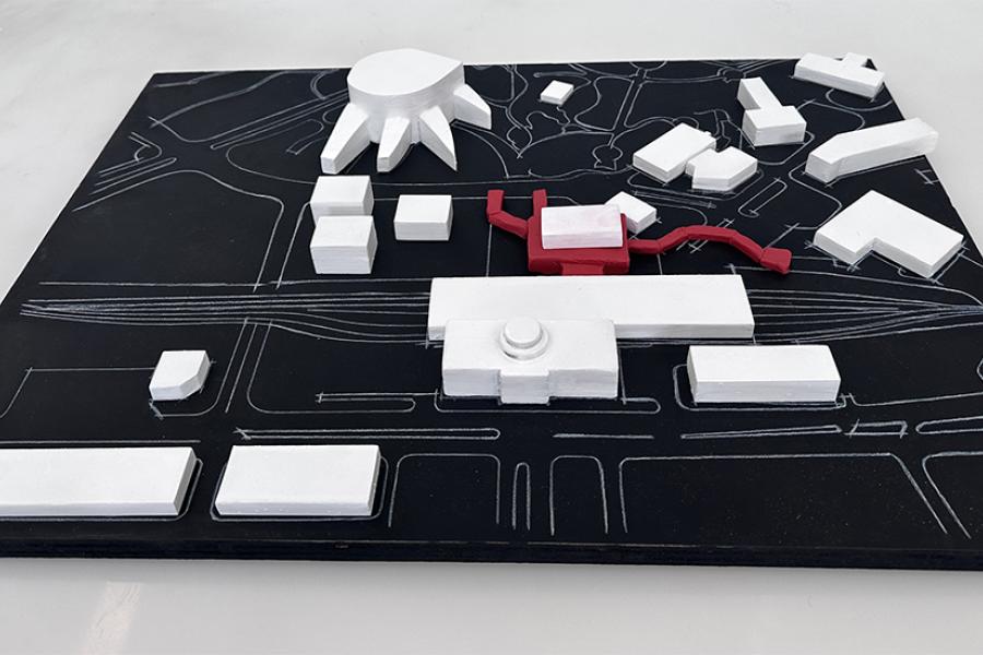 A black architectural model featuring white angular structures and roads, with a striking red serpentine pathway at the center, conveying modernity and creativity.