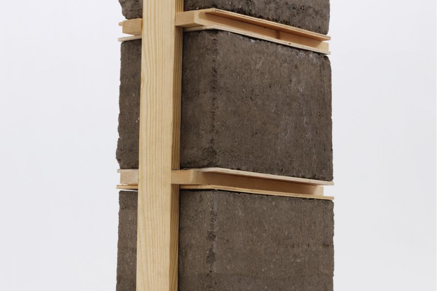 A stack of gray cement blocks is vertically supported by a wooden frame with horizontal beams. The simple, industrial design evokes stability and strength.