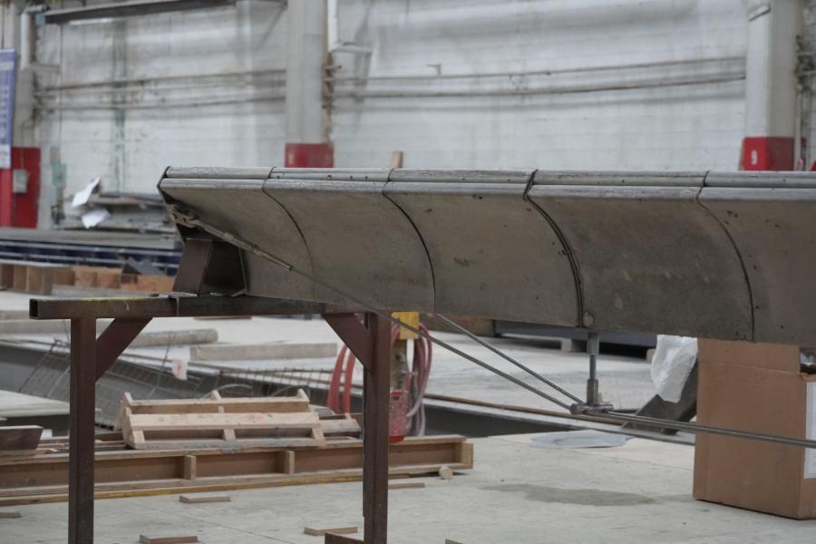 A large, industrial metal panel supported by a frame in a workshop. The space is cluttered, suggesting ongoing construction or manufacturing.
