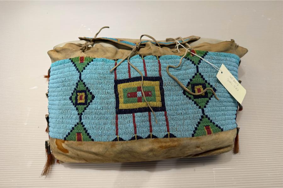 A vibrant beaded pouch with intricate geometric patterns in teal, red, green, and yellow on a light brown leather background.
