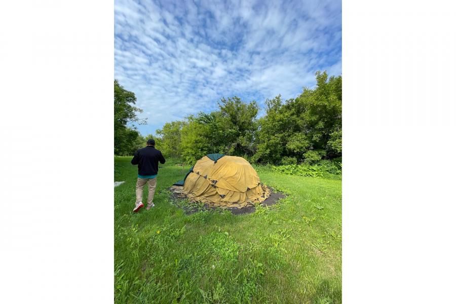 Man walking in the forest with a pile of dirt covered by a yellow blanket besides him.