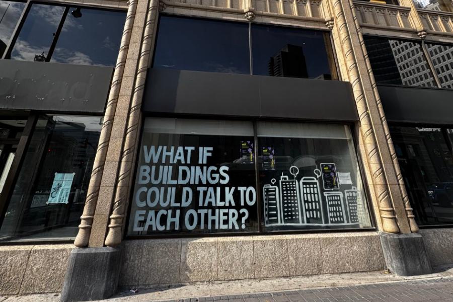 Storefront window with bold text "What if buildings could talk to each other?" next to simple line drawings of skyscrapers.