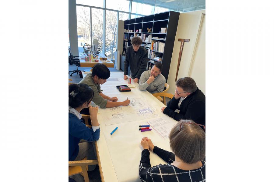 A group of six people sits around a table engaged in a collaborative meeting.