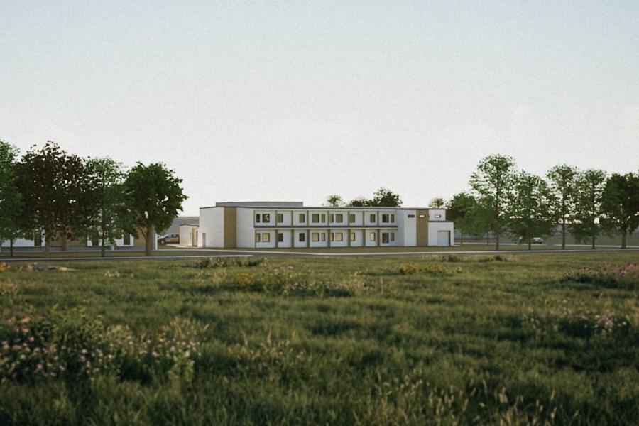 A modern, low-rise building surrounded by lush trees stands in the background of a vast, sunlit grassy field, conveying a sense of tranquility and openness.