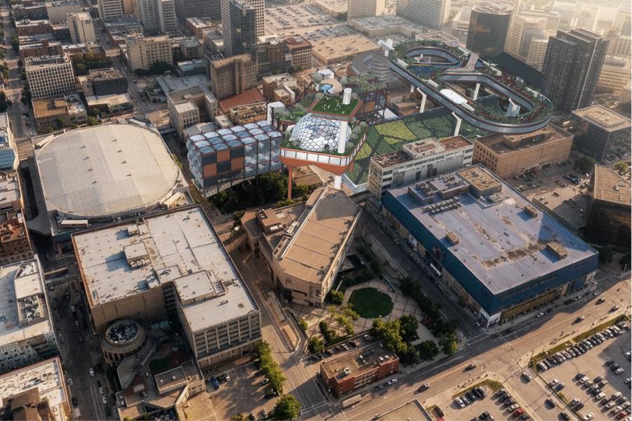 Aerial view of a cityscape with a modern architectural complex featuring green rooftops, geometric designs, and elevated structures, surrounded by urban buildings.