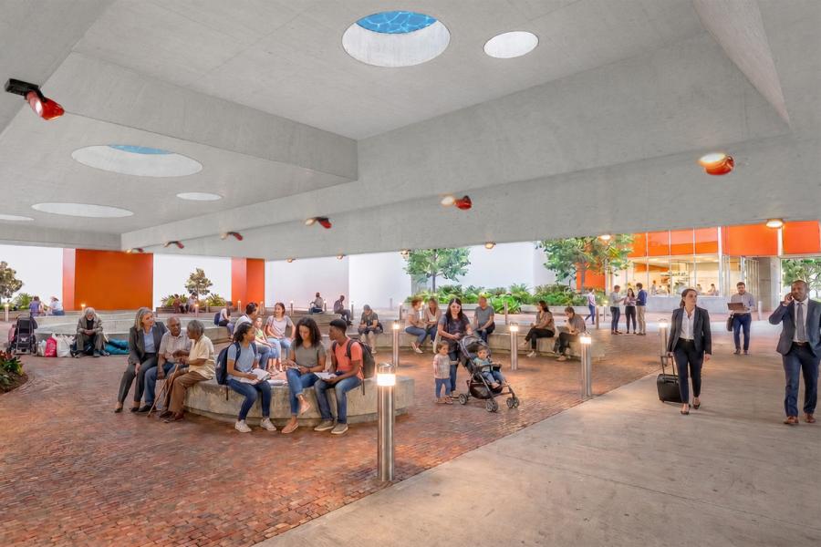 People sit on benches and walk through a covered, open-air plaza with circular skylights. 