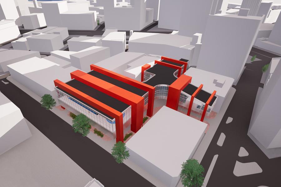 Aerial view of a modern architectural model featuring bold red and black structures with glass facades, situated among urban buildings and streets.