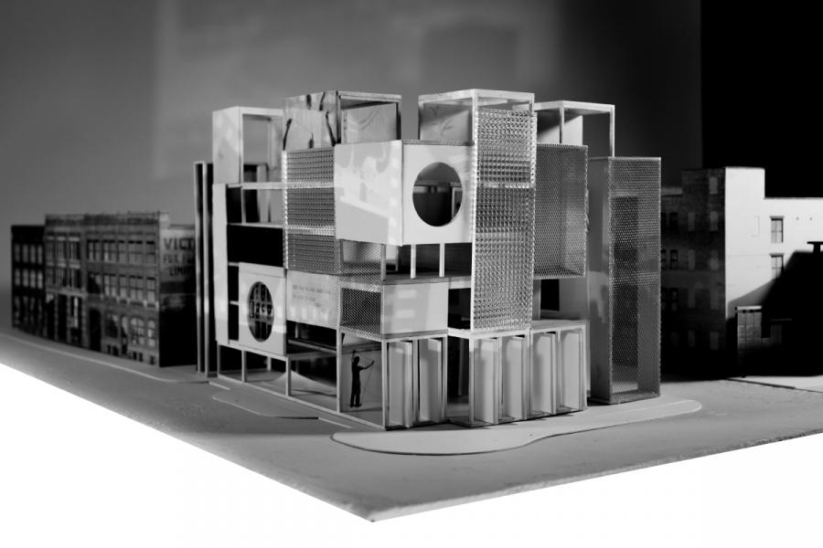Architectural model showcasing a modern building with geometric forms, circular cutouts, and textured surfaces, set among traditional structures.